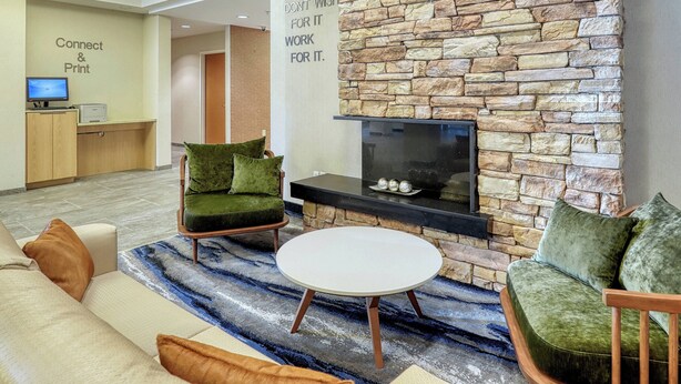 A modern lounge area with a stone wall, a flat-screen TV, and comfortable seating. - Fairfield Inn & Suites by Marriott Woodbridge (Avenel)