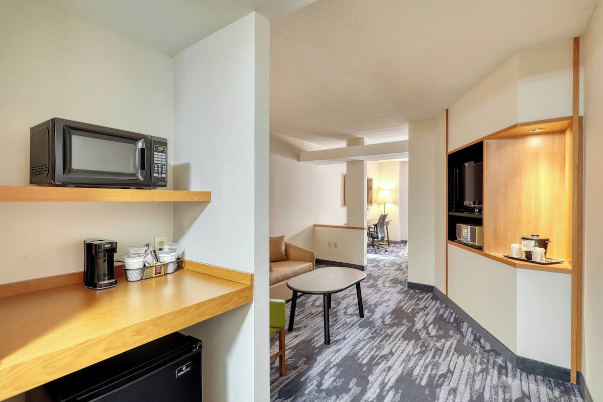 A hotel room with a kitchenette, a microwave, a coffee maker, a small table, and a sofa.