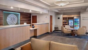 A hotel reception area with a reception desk, a Corner Market vending machine, and a seating area with chairs and a table. - Fairfield Inn & Suites by Marriott Woodbridge (Avenel)
