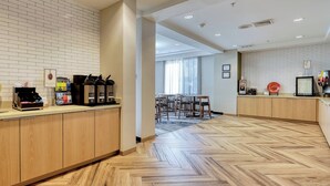 A hotel lobby with a herringbone wood floor, a reception desk with coffee machines, and a dining area with chairs and tables. - Fairfield Inn & Suites by Marriott Woodbridge (Avenel)