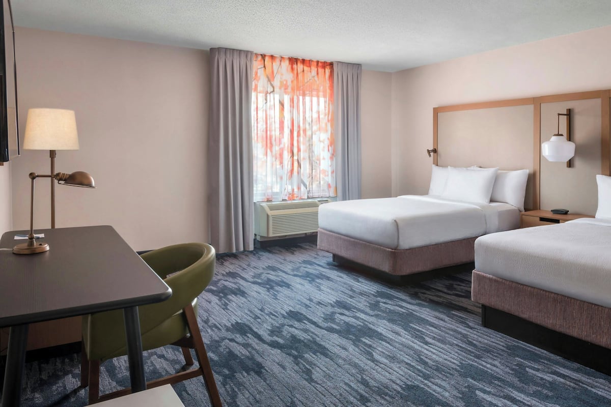 A hotel room with two beds, a desk, a chair, and a window with curtains.