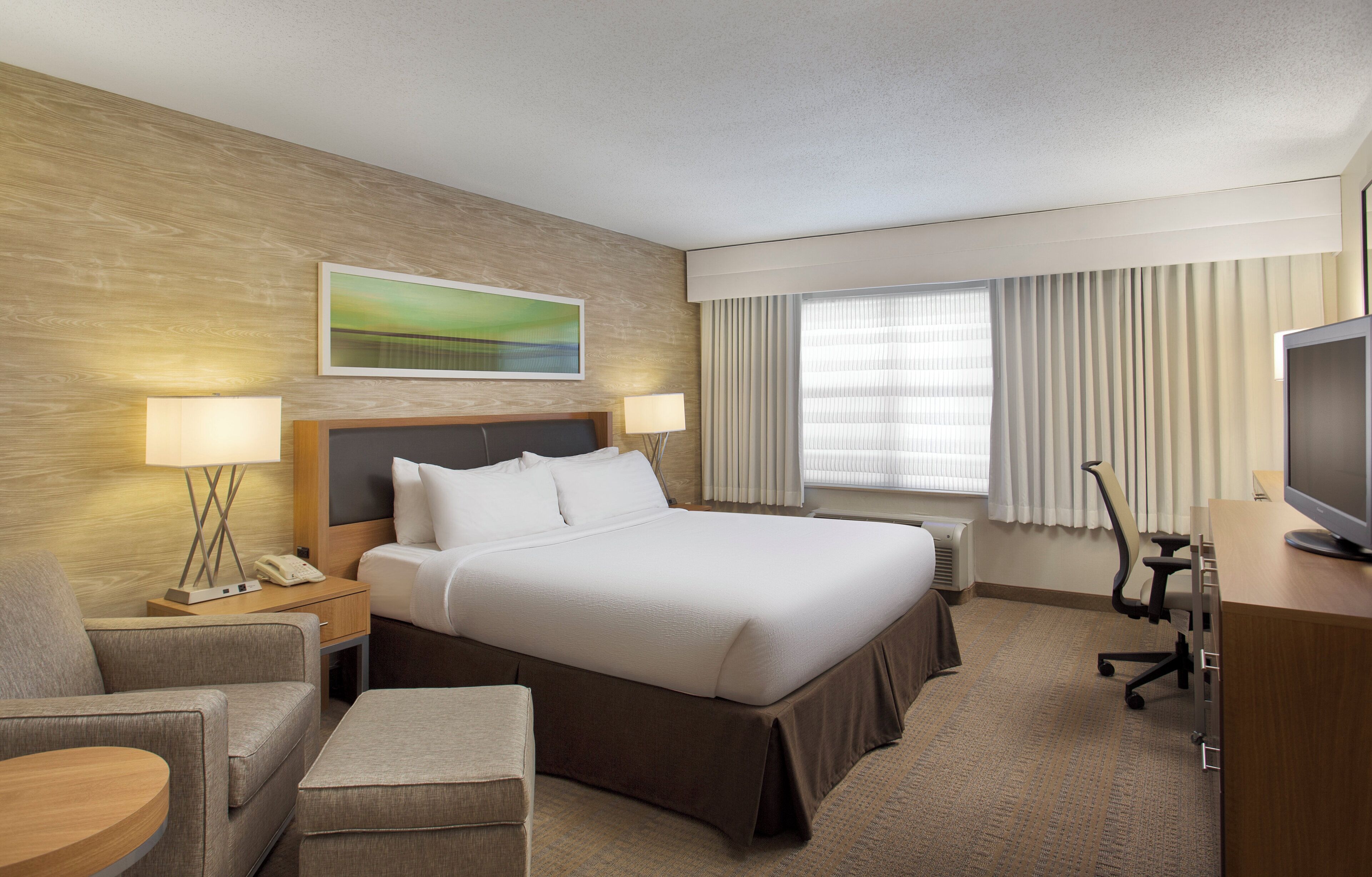 A hotel room with a bed, bedside tables, a desk with a chair, a television, and a window with curtains.