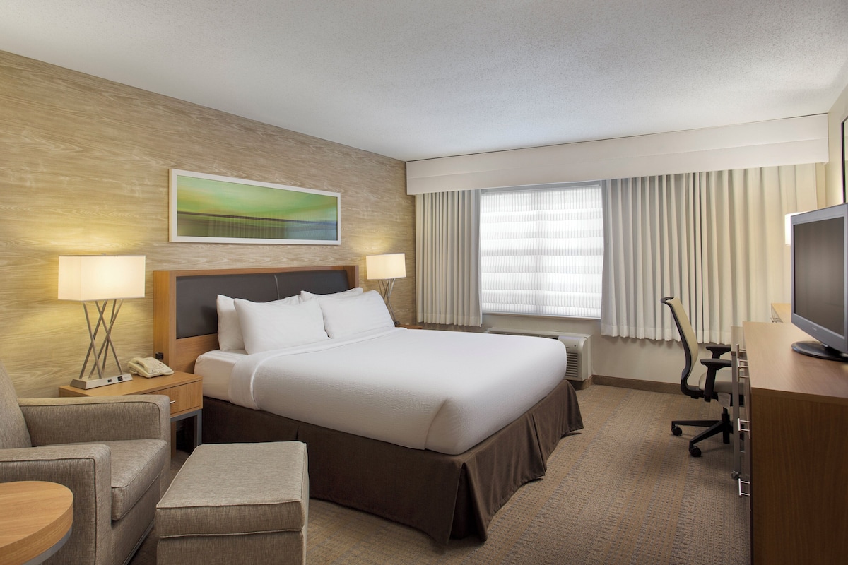 A hotel room with a bed, bedside tables, a desk with a chair, a television, and a window with curtains.