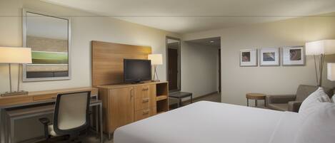 A hotel room with a bed, desk, chair, television, and artwork on the walls.