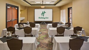 Ein Konferenzraum mit Tischen und Stühlen, einer Projektionsleinwand mit dem Holiday Inn Logo und einem Teppichboden.