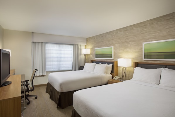 A hotel room with two beds, a desk with a computer, a lamp, and a window with curtains.