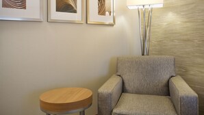 A room with a grey armchair, a round wooden table, and three framed artworks on the wall.