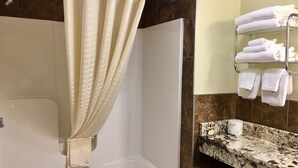 A bathroom with a bathtub, a shower curtain, a towel rack with folded towels, and a granite countertop. - Scottish Inn Sturbridge (Sturbridge)