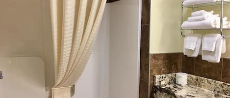Une salle de bain avec une baignoire, un rideau de douche, un porte-serviettes avec des serviettes pliées et un comptoir en granit.
