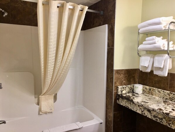 Un baño con bañera, cortina de ducha, toallero con toallas dobladas y encimera de granito.