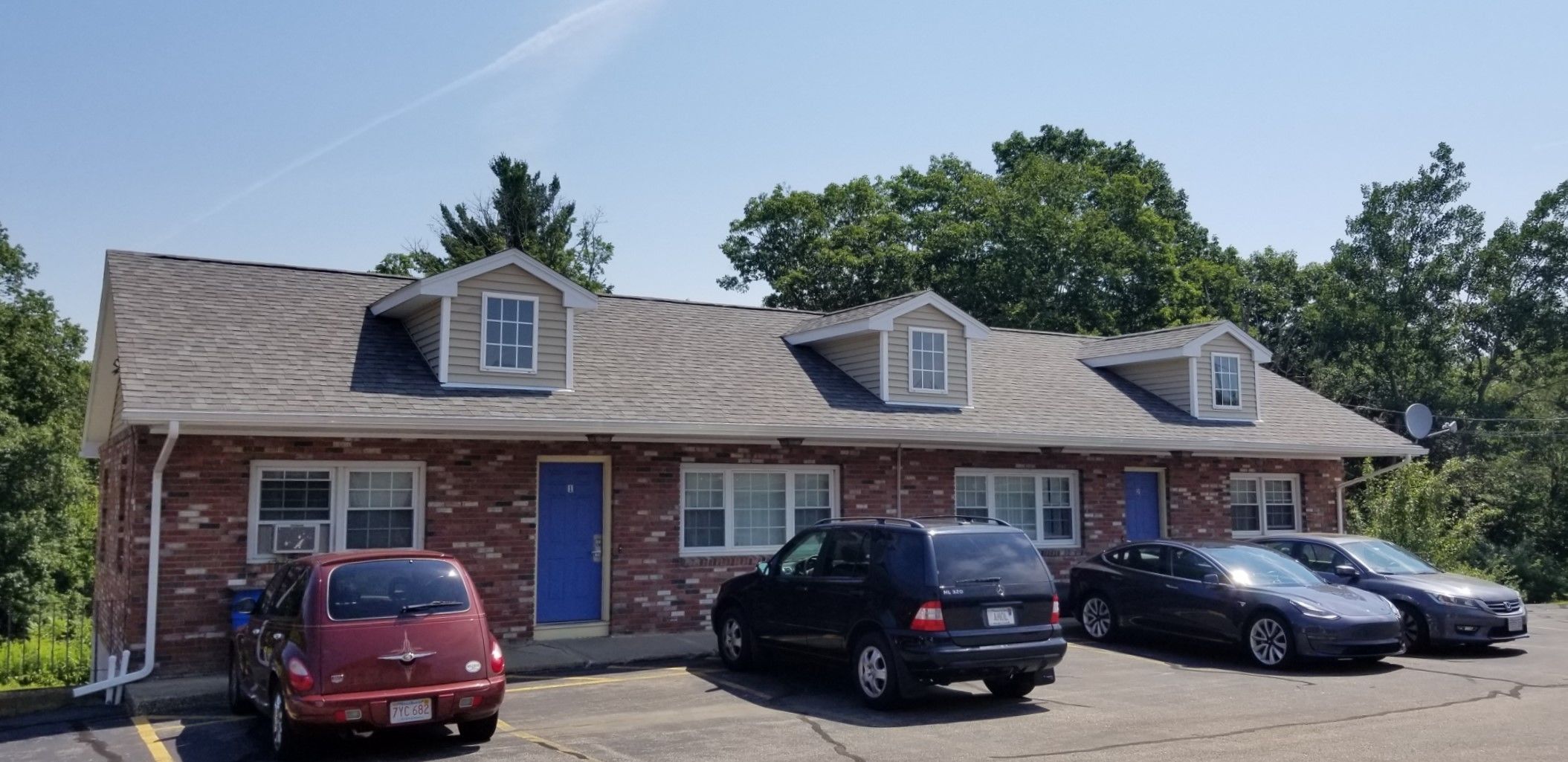 A two-story motel with a brick facade and a flat roof. There are four cars parked in front.