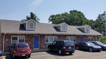 A two-story motel with a brick facade and a flat roof. There are four cars parked in front.