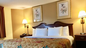 A hotel room with a large bed, two bedside lamps, a nightstand with a phone, and two framed floral paintings on the wall. - Scottish Inn Sturbridge (Sturbridge)
