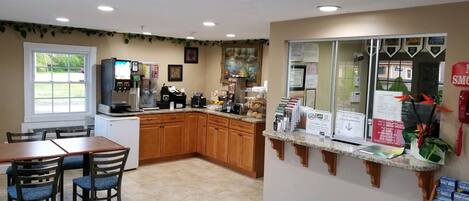 A kitchen with wooden cabinets, a coffee machine, and a refrigerator. There is a window with a view of a parking lot.