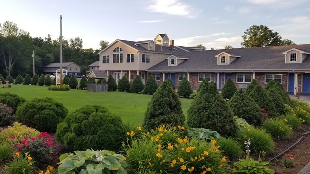 A large building with multiple windows and a well-maintained garden with various plants and flowers. - Scottish Inn Sturbridge (Sturbridge)