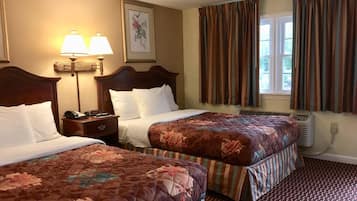 A hotel room with two beds, a nightstand with a phone, a lamp, and a framed picture on the wall.