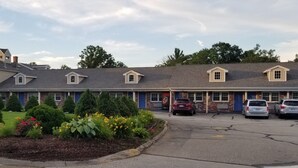 A motel with multiple units, a parking lot, and landscaped gardens. - Scottish Inn Sturbridge (Sturbridge)