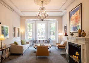 A spacious living room with a fireplace, a chandelier, and a view through large windows. - Newbury Guest House (Boston)
