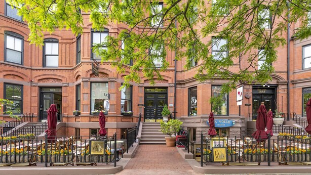 A brick building with a central entrance, outdoor seating area with tables and chairs, and a sign for 'A Voile CANNES'. - Newbury Guest House (Boston)