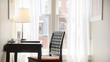 A room with a desk, chair, lamp, and a window with curtains.