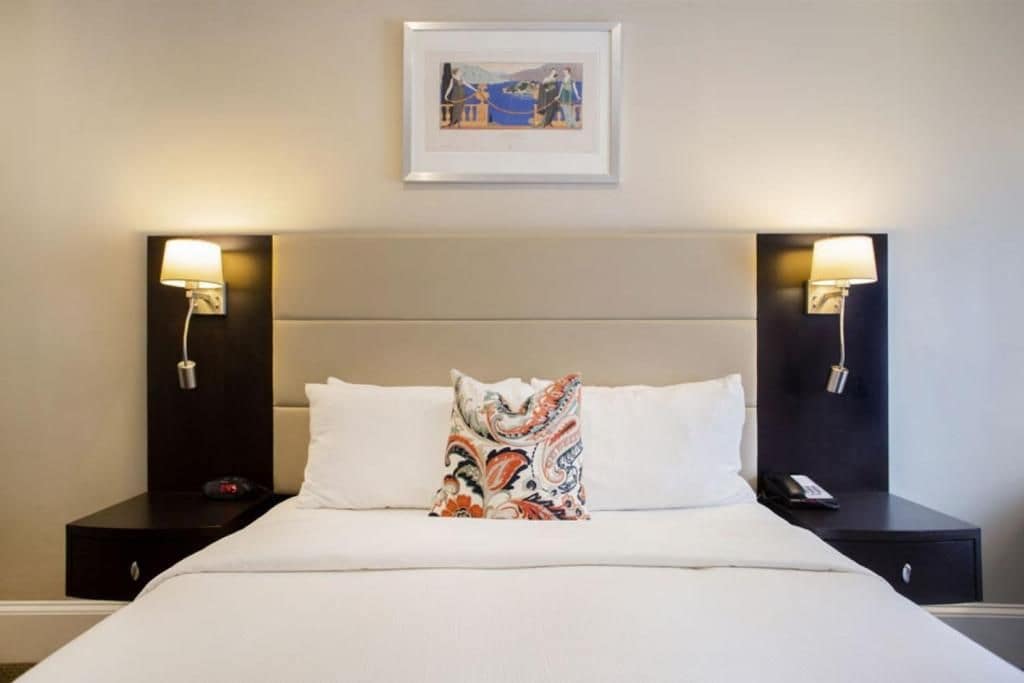Habitación de hotel con cama, dos mesitas de noche, una lámpara y un cuadro en la pared.