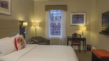 Habitación de hotel con una cama grande, un escritorio con silla, televisión y ventana con vista a edificios.