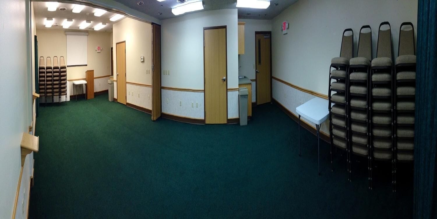 A conference room with a green carpet, a whiteboard, a projector screen, and a table with chairs.