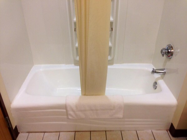 Una bañera blanca con una toalla colgada al borde, un grifo cromado y una alcachofa de ducha visible tras una cortina.