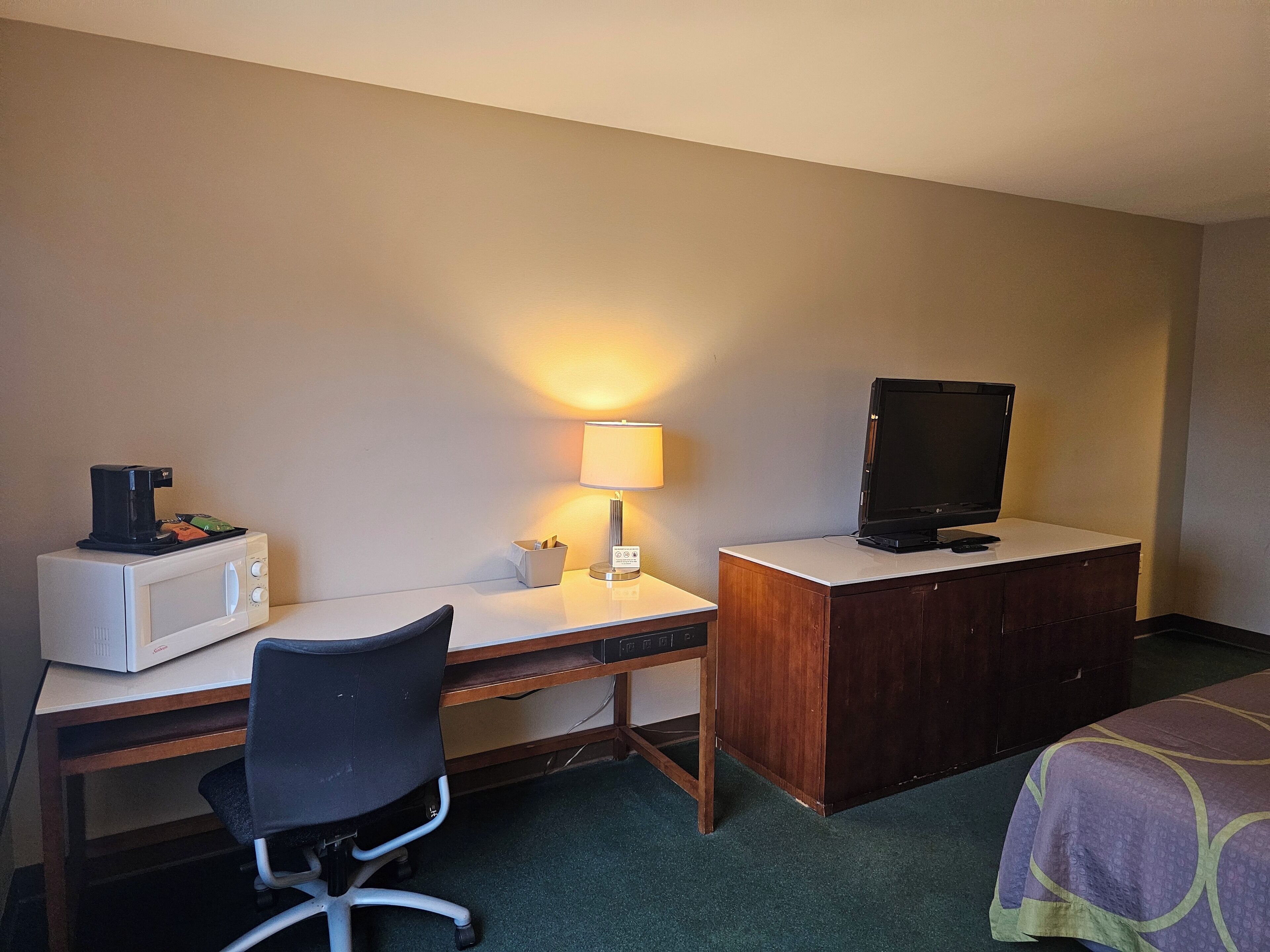 Une chambre d’hôtel équipée d’un bureau, d’un four à micro-ondes, d’une télévision, d’une chaise et d’un lit.