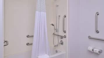 A bathroom with a bathtub, shower, grab bars, and a toilet paper holder.