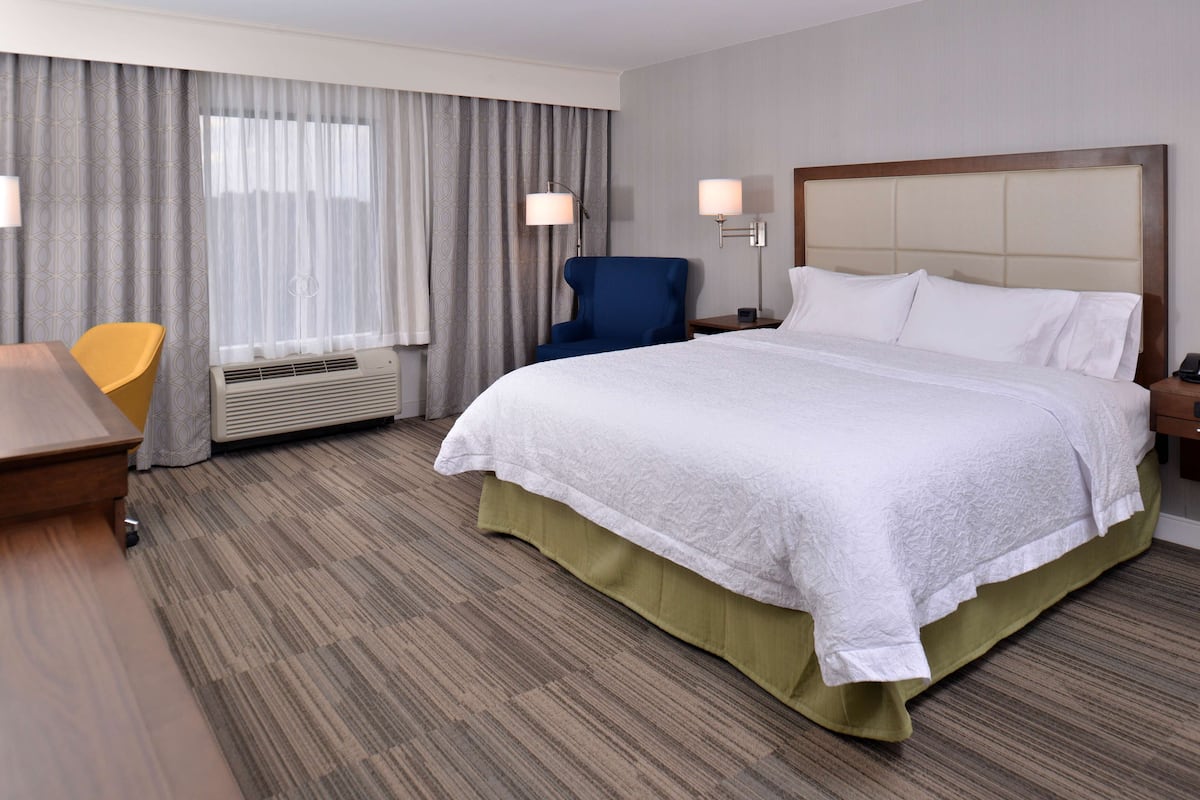 A hotel room with a large bed, a desk, a chair, and a window with curtains.