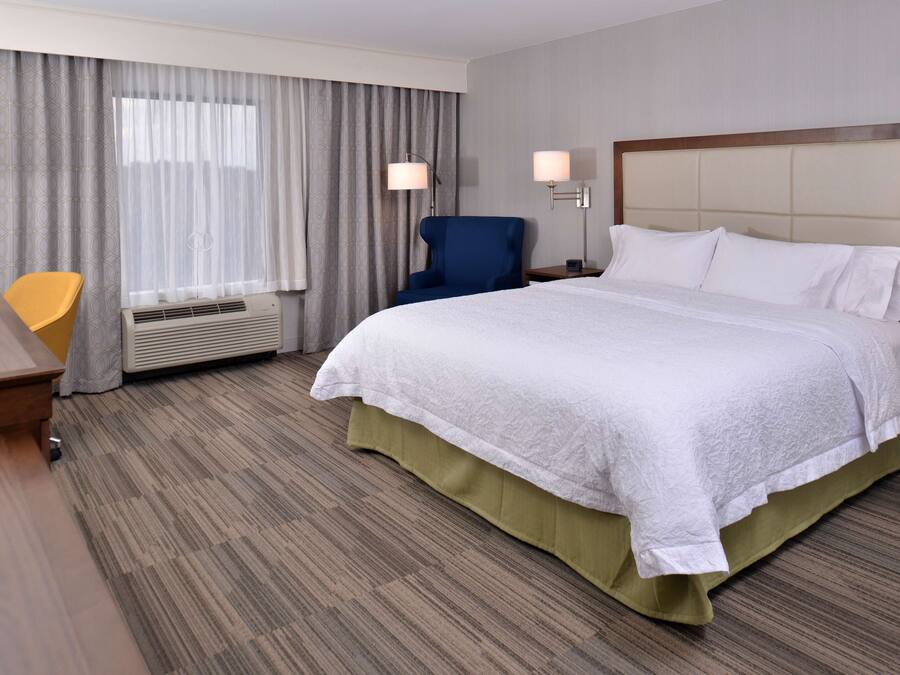 A hotel room with a large bed, a desk, a chair, and a window with curtains.