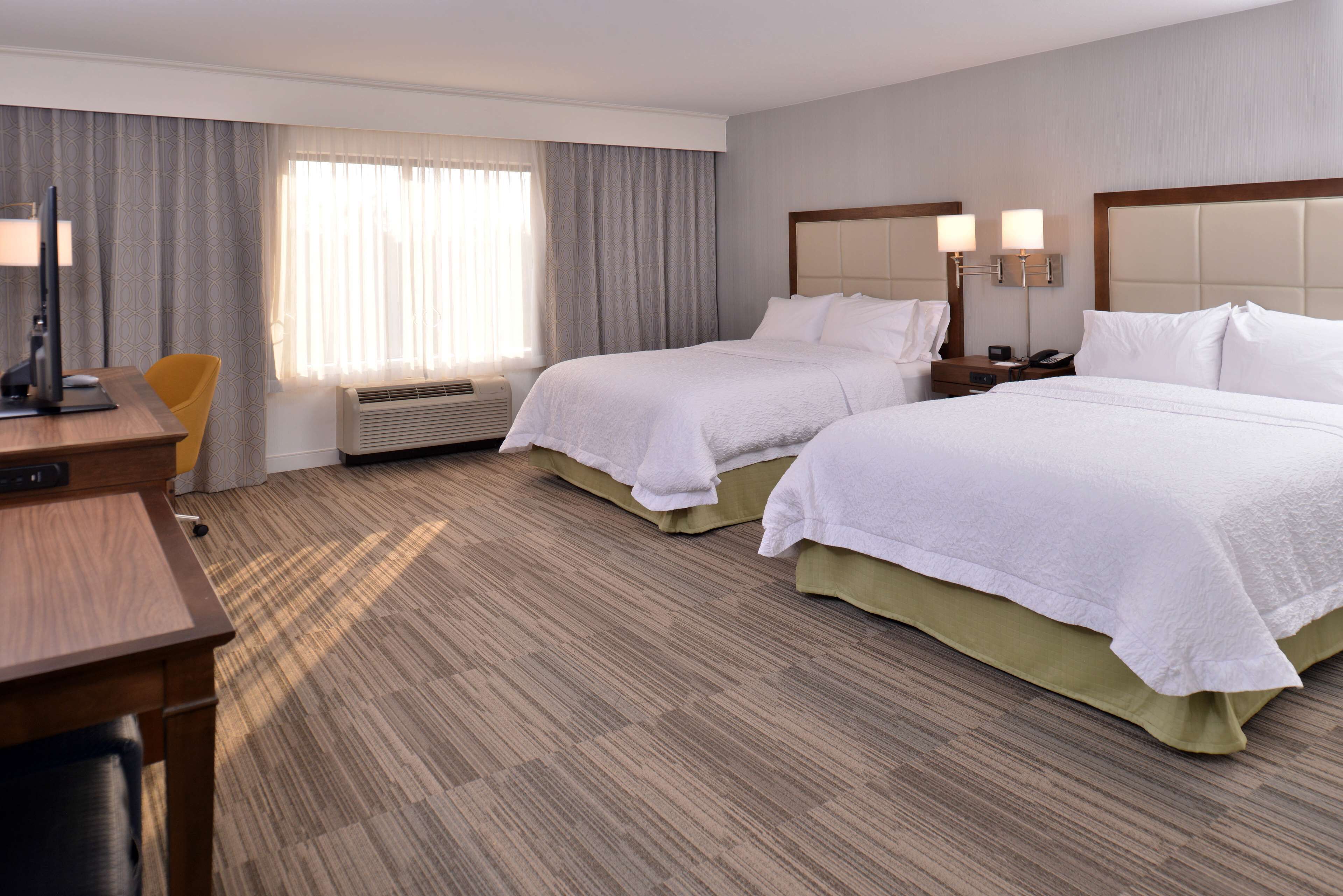 Habitación de hotel con dos camas, un escritorio, una silla y un ventanal con cortinas.