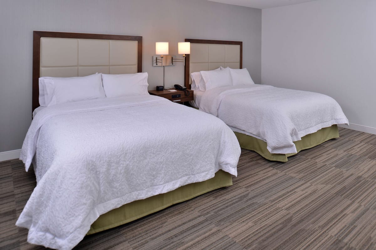 A hotel room with two beds, a nightstand with a lamp, and a wooden headboard.
