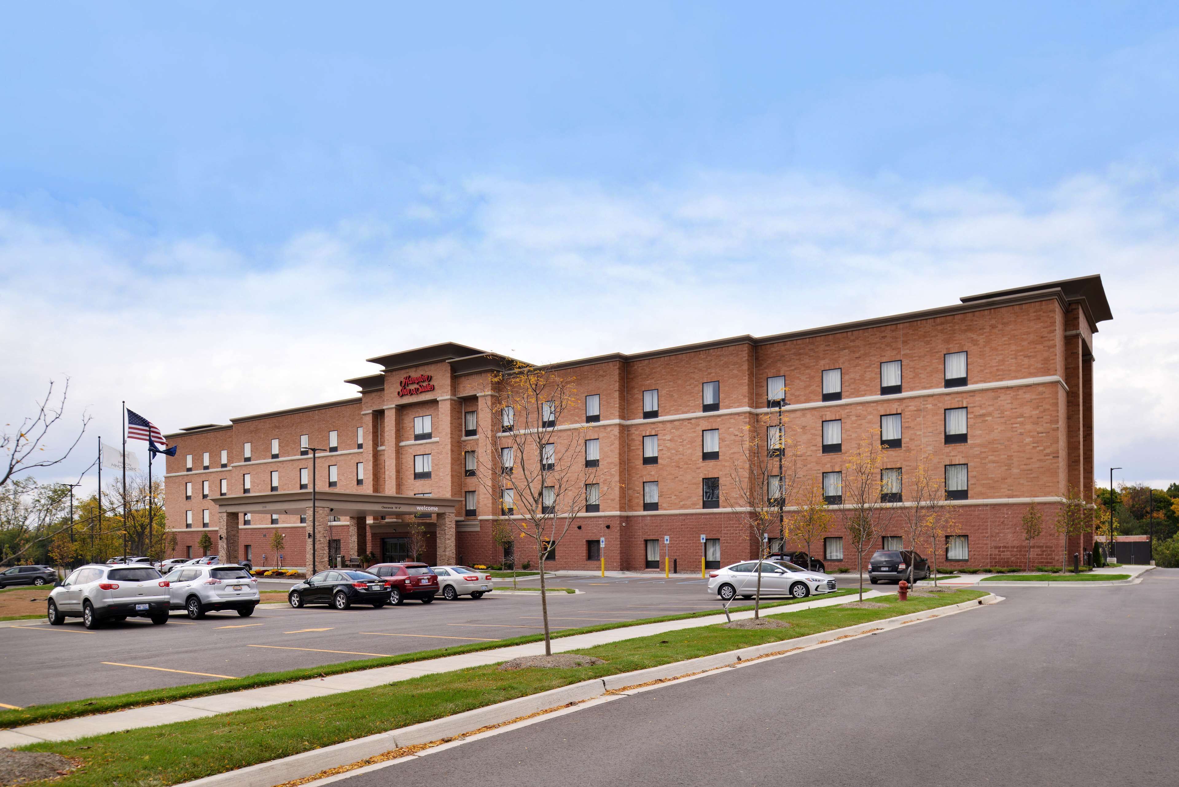 A multi-story hotel with a brick facade, a parking lot with several cars, and a flagpole with an American flag.