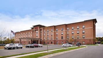 A multi-story hotel with a brick facade, a parking lot with several cars, and a flagpole with an American flag.