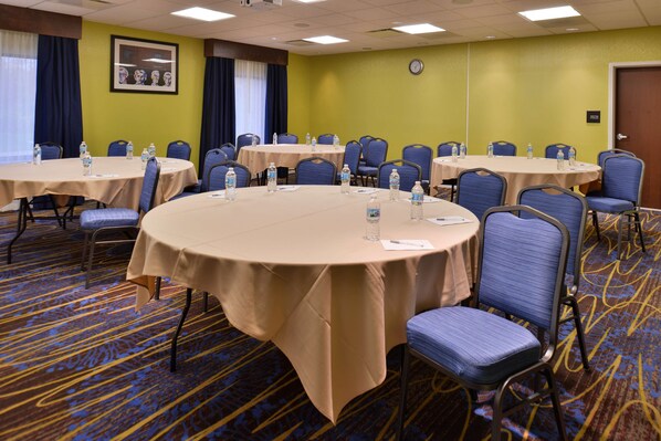 A conference room with multiple round tables, each with chairs and water bottles.
