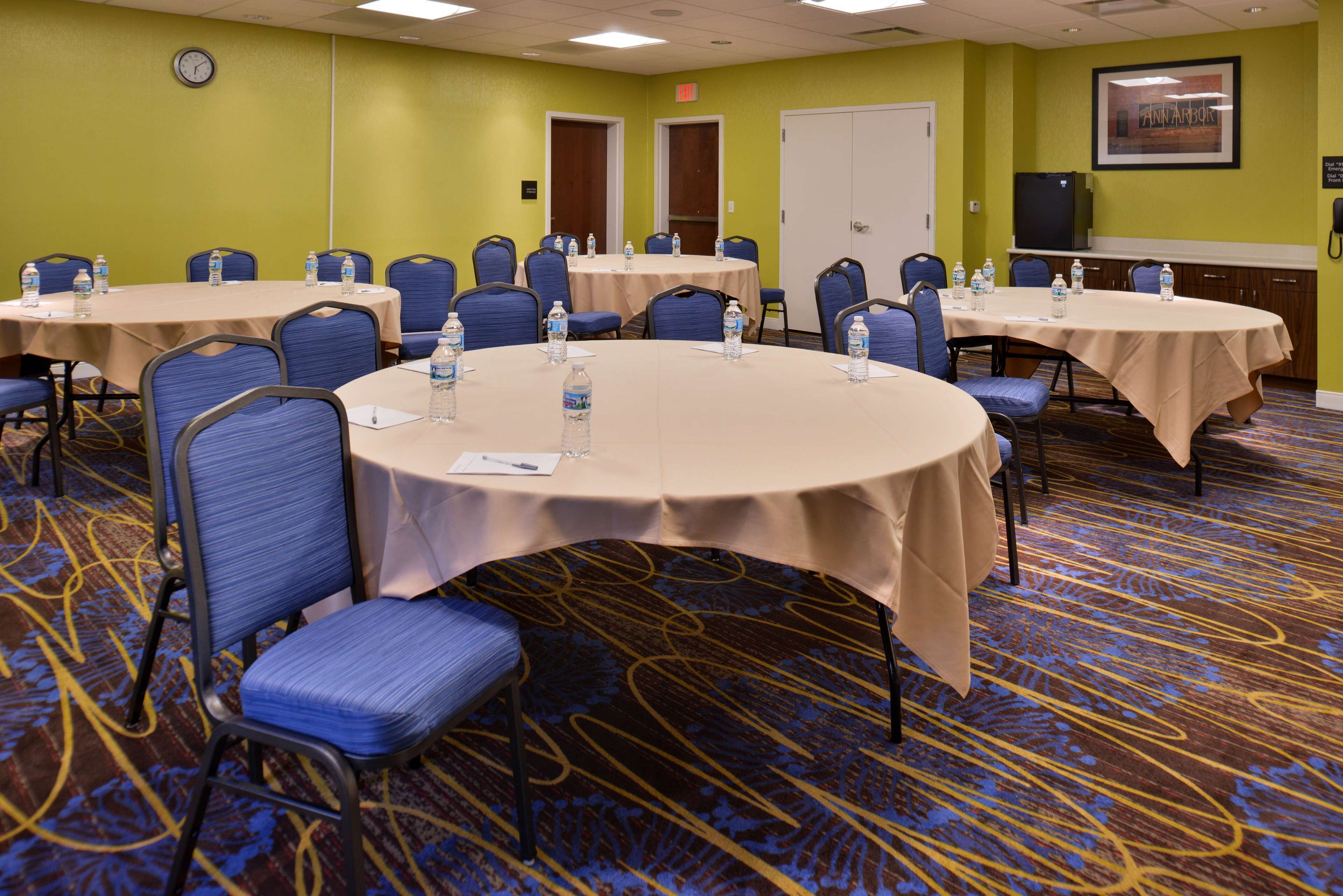 A conference room with round tables, blue chairs, water bottles, and a clock on the wall.