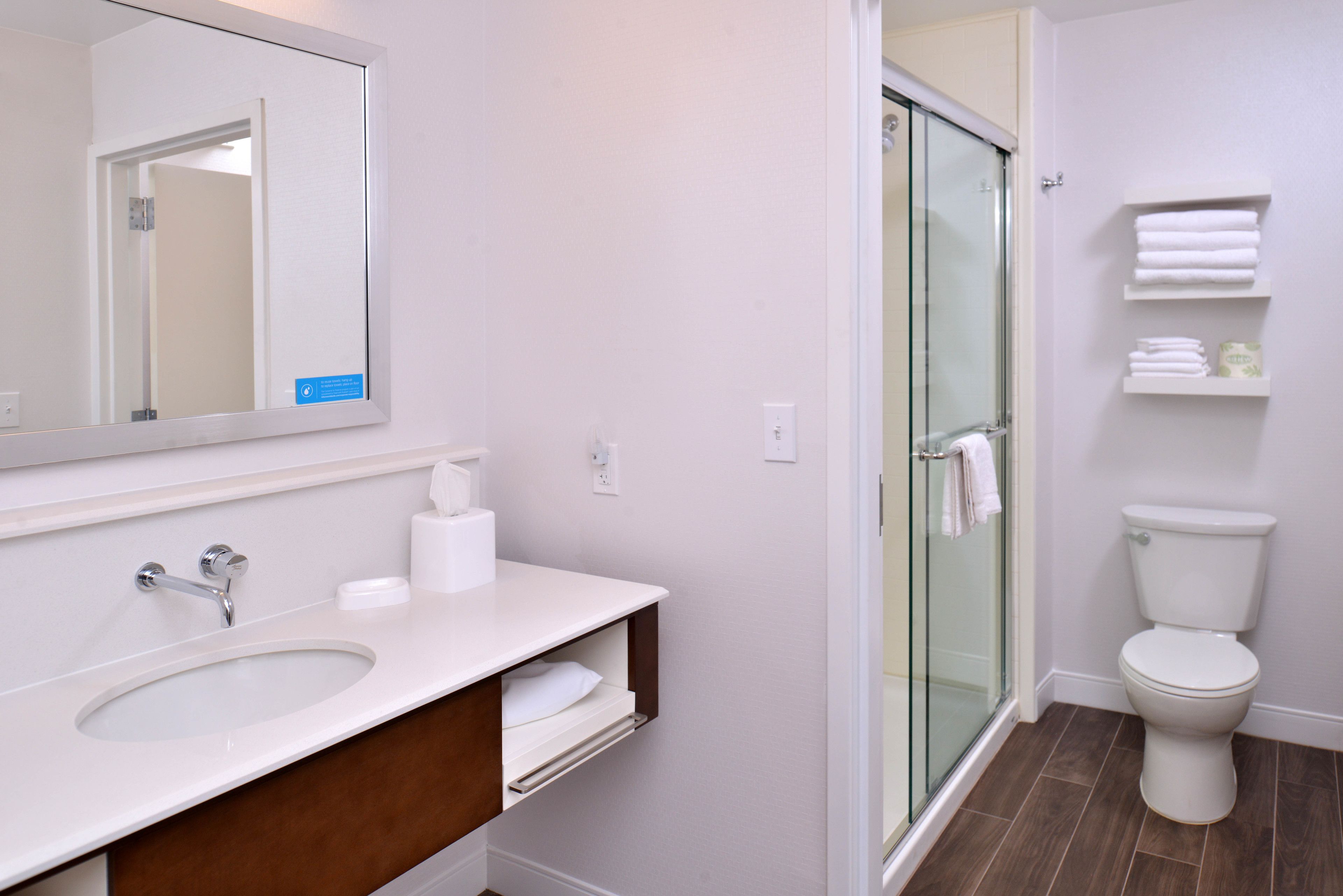 A modern bathroom with a glass-enclosed shower, a white sink with a mirror above it, and a toilet with a glass door.