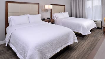 Habitación de hotel con dos camas, una mesita de noche con lámpara y un ventanal con cortinas.