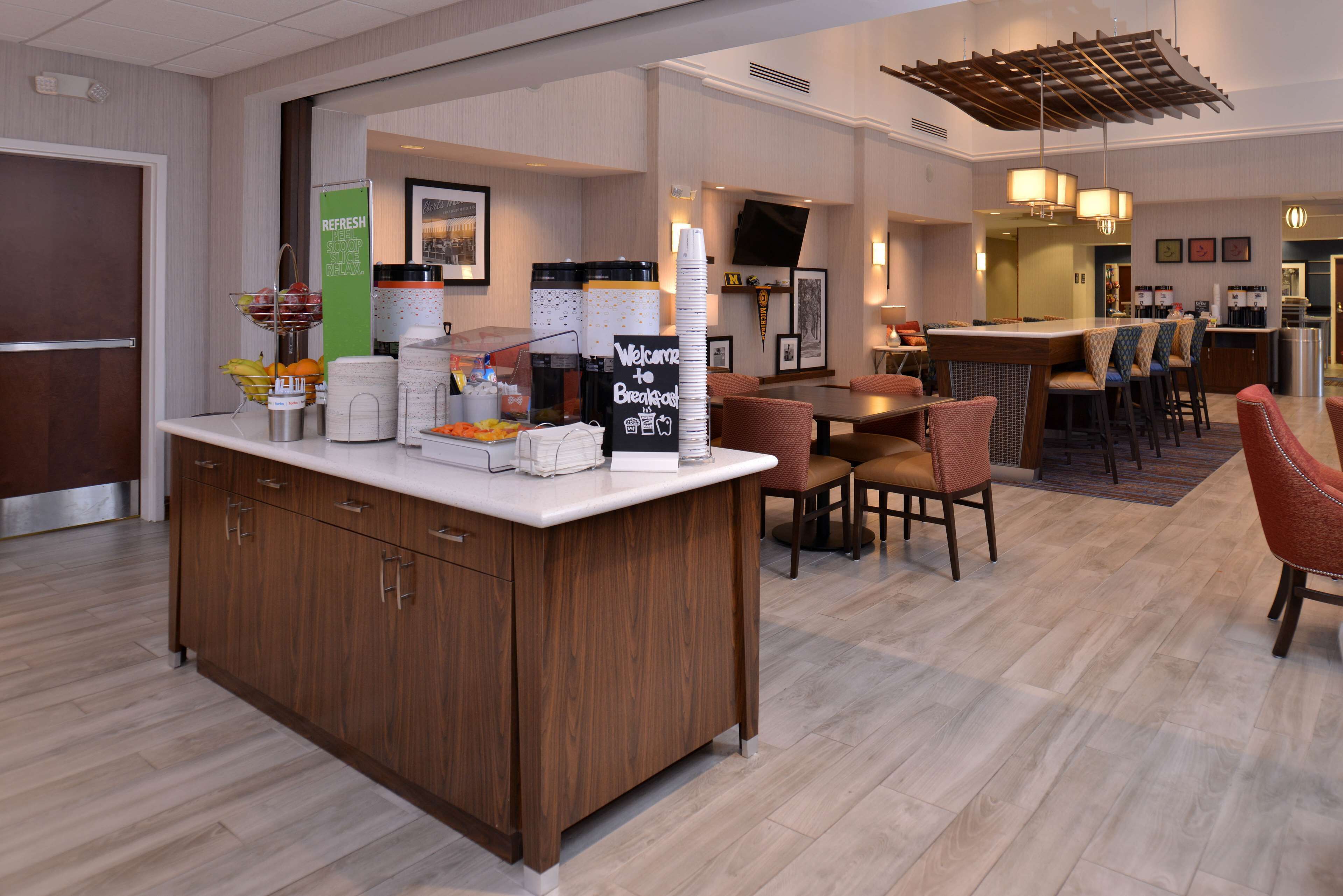 A hotel breakfast area with a wooden counter, bar seating, and a buffet setup.