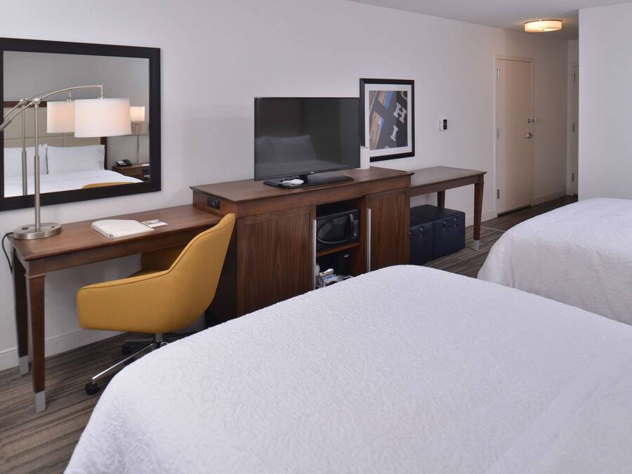 A hotel room with two beds, a desk with a computer, a chair, a TV, and a mirror.
