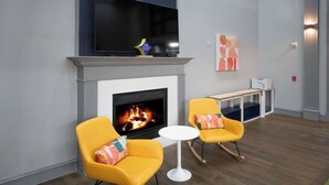 Un salon moderne avec une cheminée, deux fauteuils à bascule jaunes, une table ronde blanche et un téléviseur à écran plat fixé au-dessus de la cheminée.