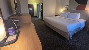 Une chambre d’hôtel avec un lit, un bureau avec un ordinateur, une chaise et une petite table sur laquelle se trouvent un sac et une bouteille.