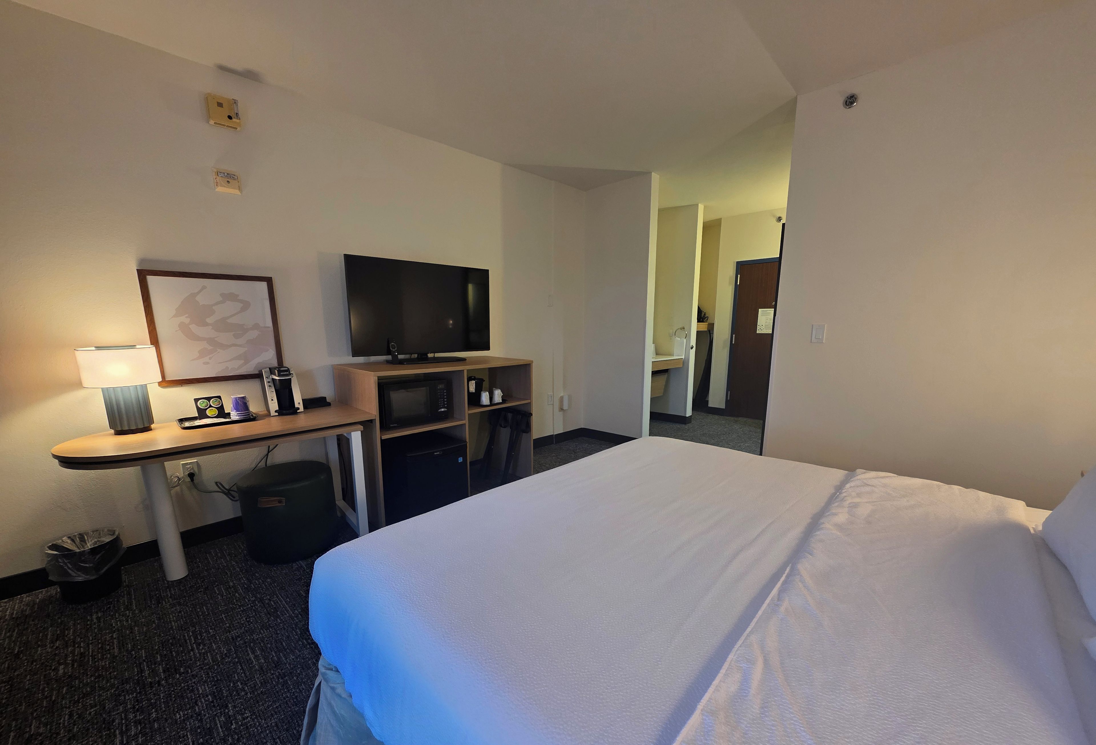 A hotel room with a bed, a desk with a lamp, a microwave, and a television.