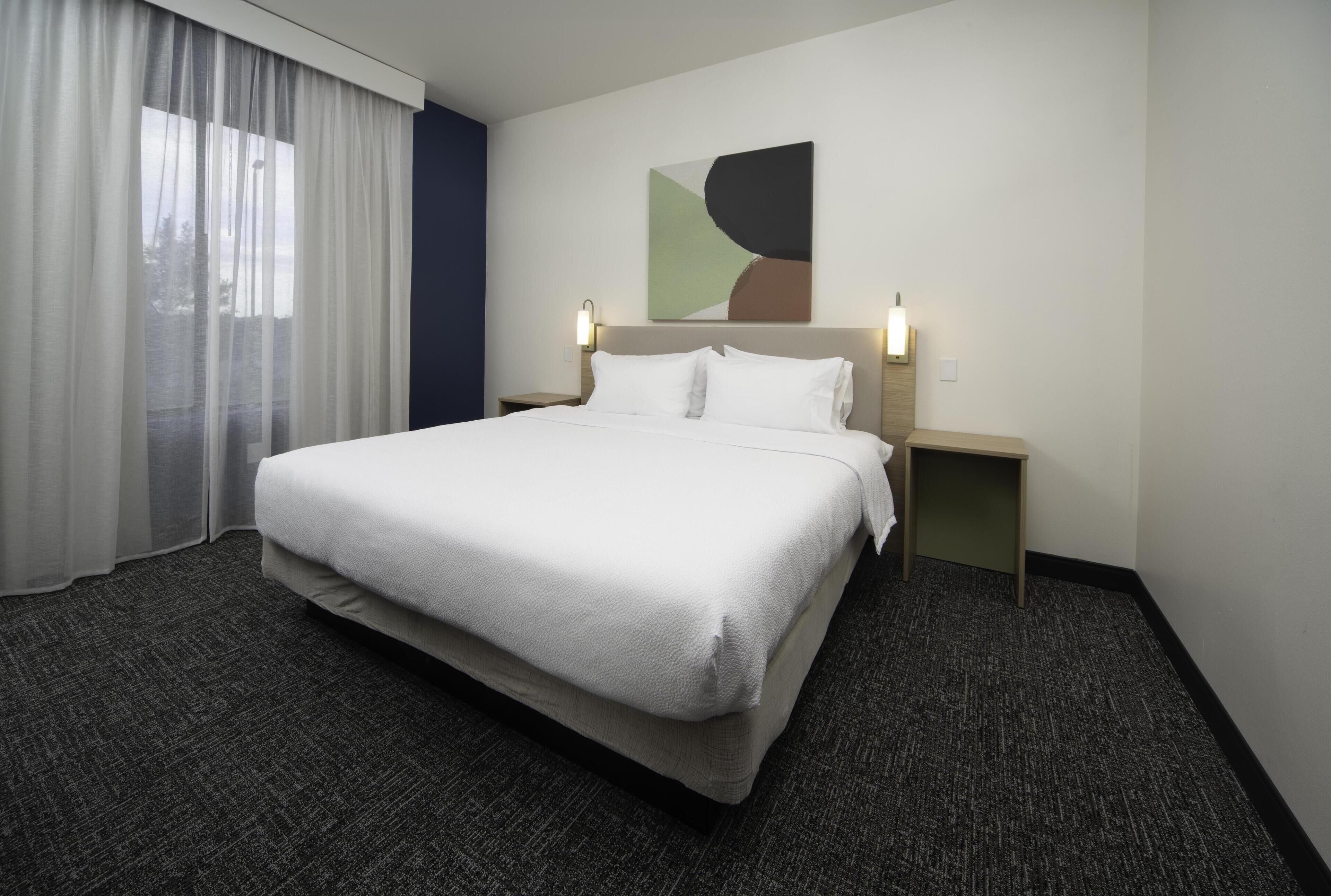 Habitación de hotel con una cama grande, una mesita de noche y un cuadro abstracto colgado en la pared.