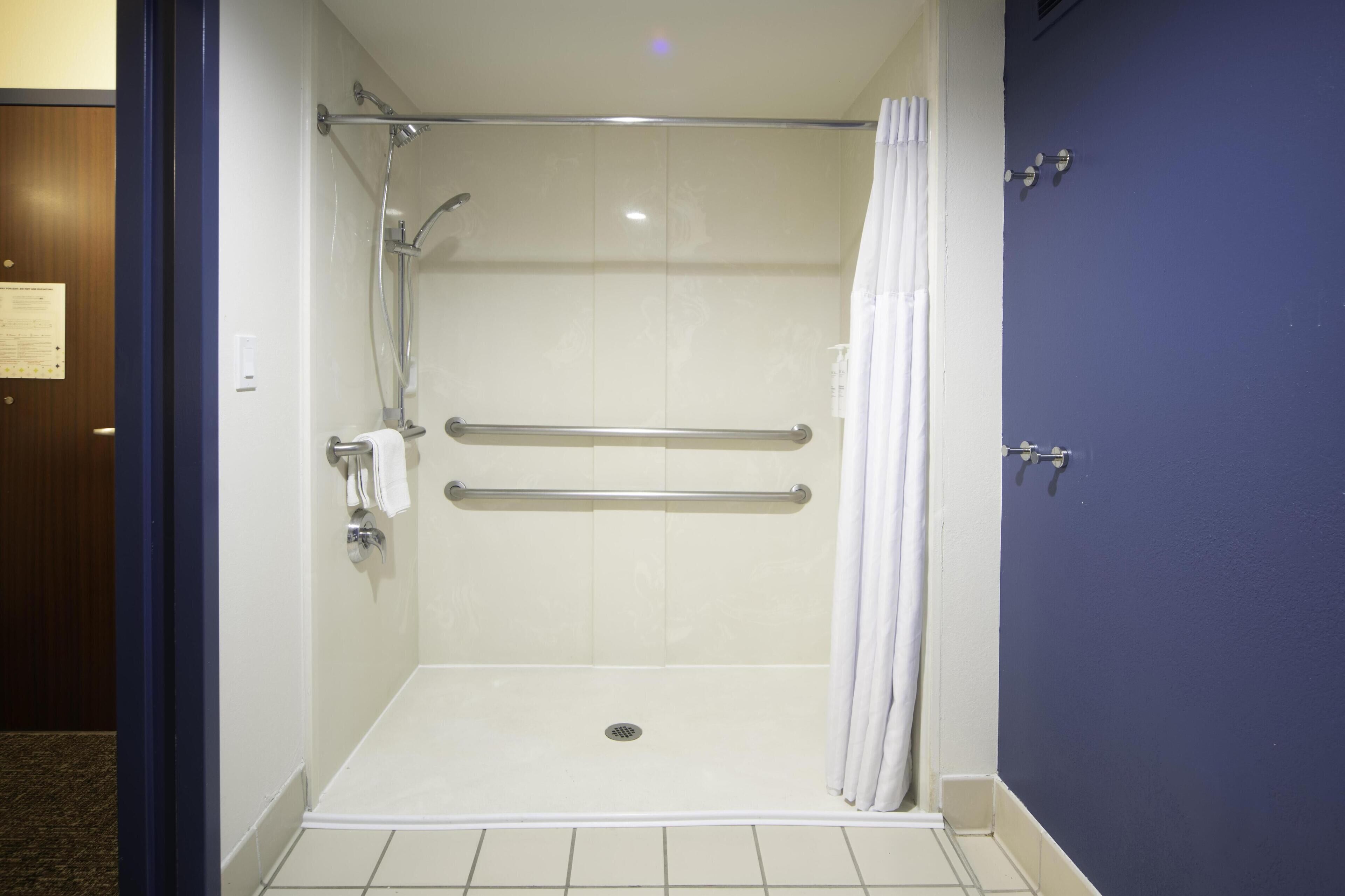 A walk-in shower with a grab bar, a white door, and a blue wall.