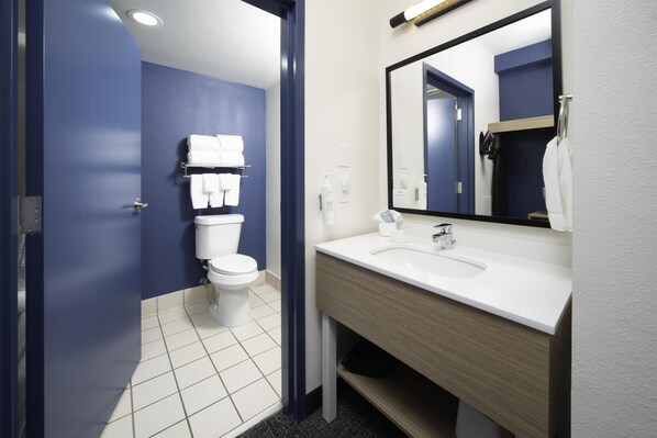 Un baño moderno con inodoro blanco, paredes azules, tocador de madera y un espejo grande.