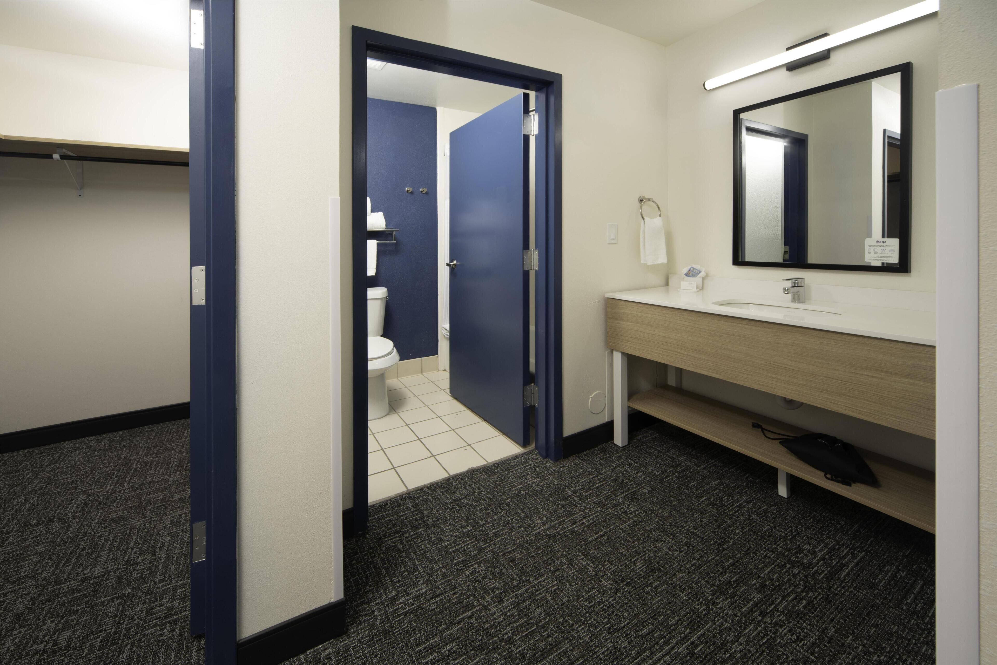 Een hotelbadkamer met toilet, wastafel, spiegel en een deur naar een andere kamer.