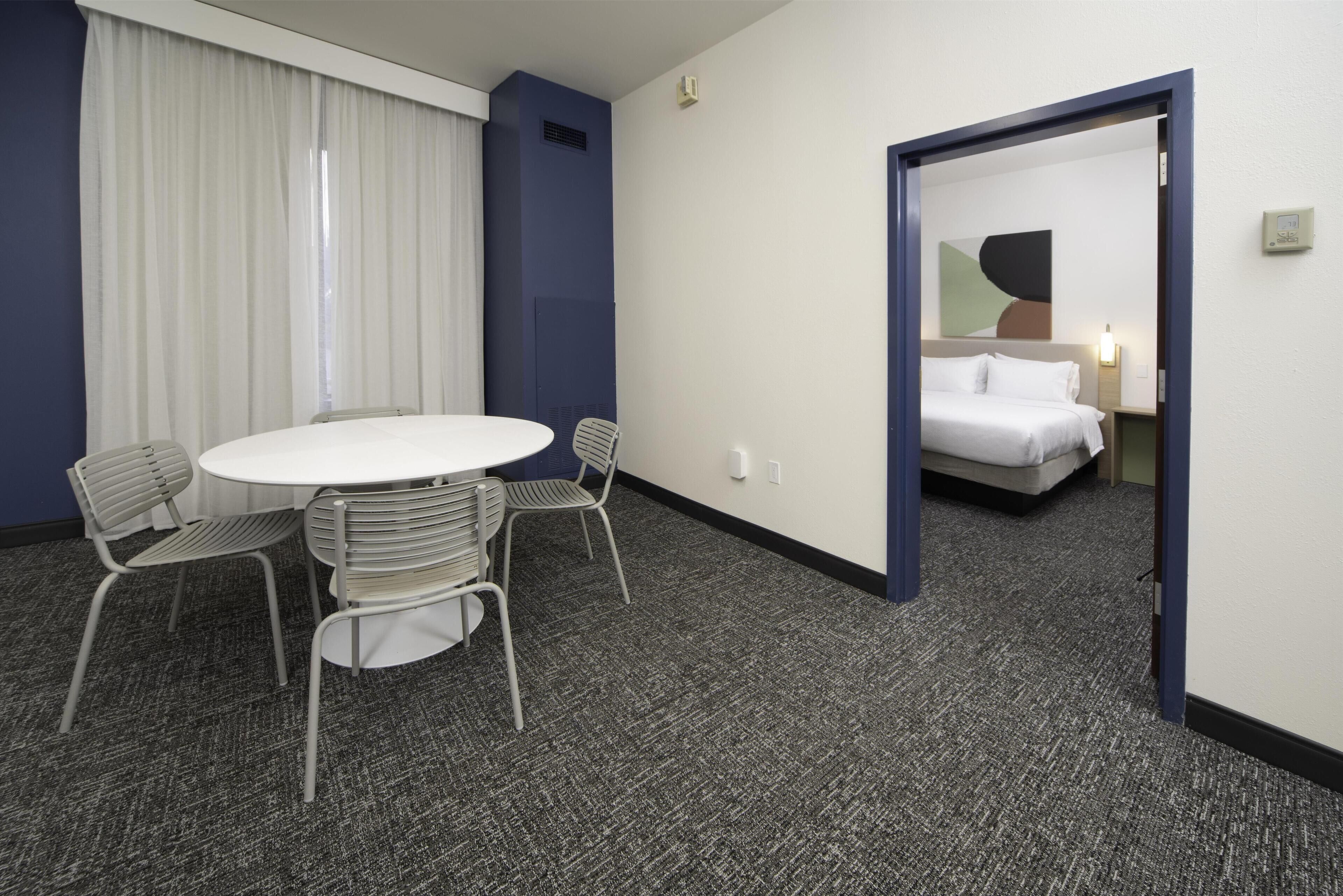 Camera d'albergo con un tavolo rotondo, due sedie, un letto e una porta che conduce a un'altra stanza.